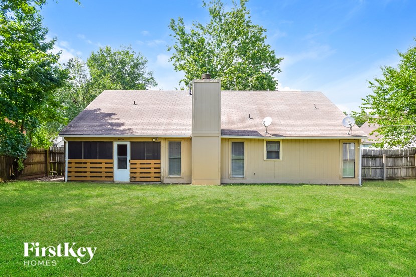 A house with a blue door and a white door is surrounded by a fence and has a grassy yard.