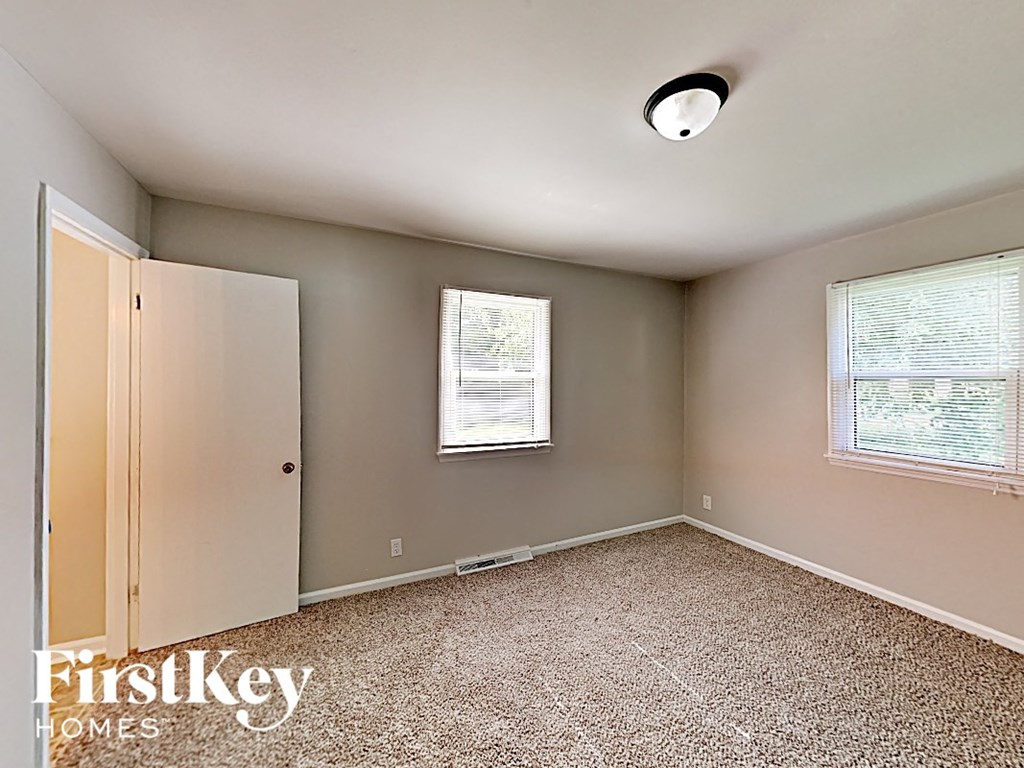 A room with a carpet floor, a window with blinds, and a door.