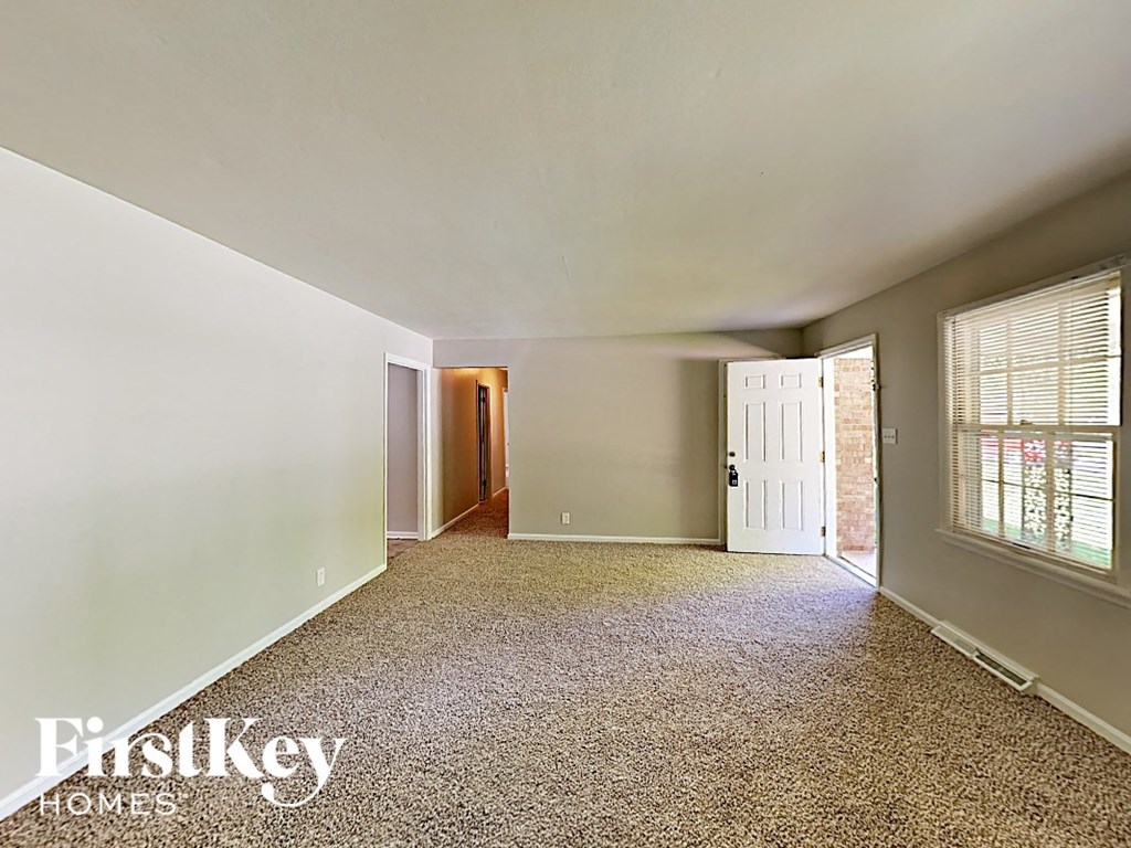 A spacious room with a carpeted floor and a window with blinds.