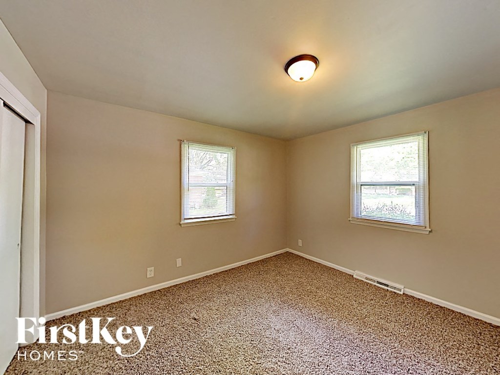 A room with a carpeted floor and two windows.