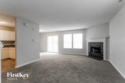 A spacious living room with a fireplace and a kitchen area in the background.