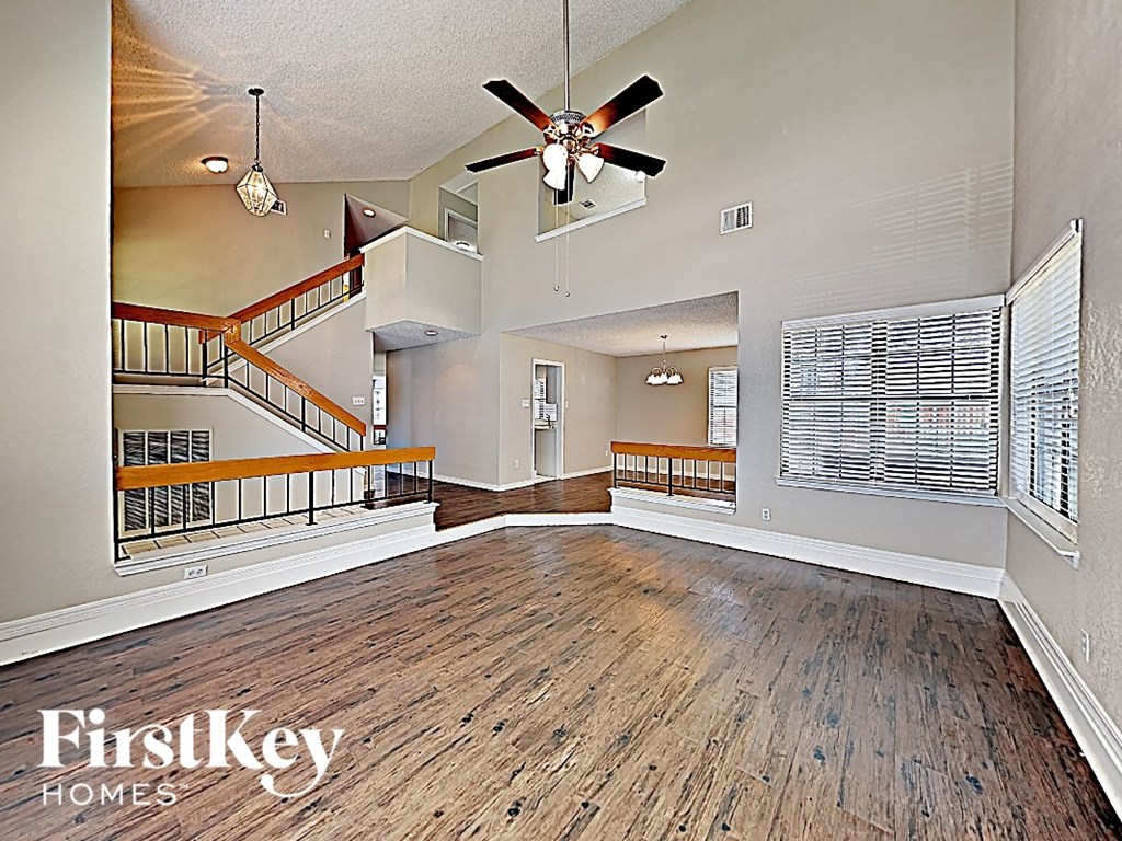 A spacious room with a wooden floor and a staircase with a metal railing.