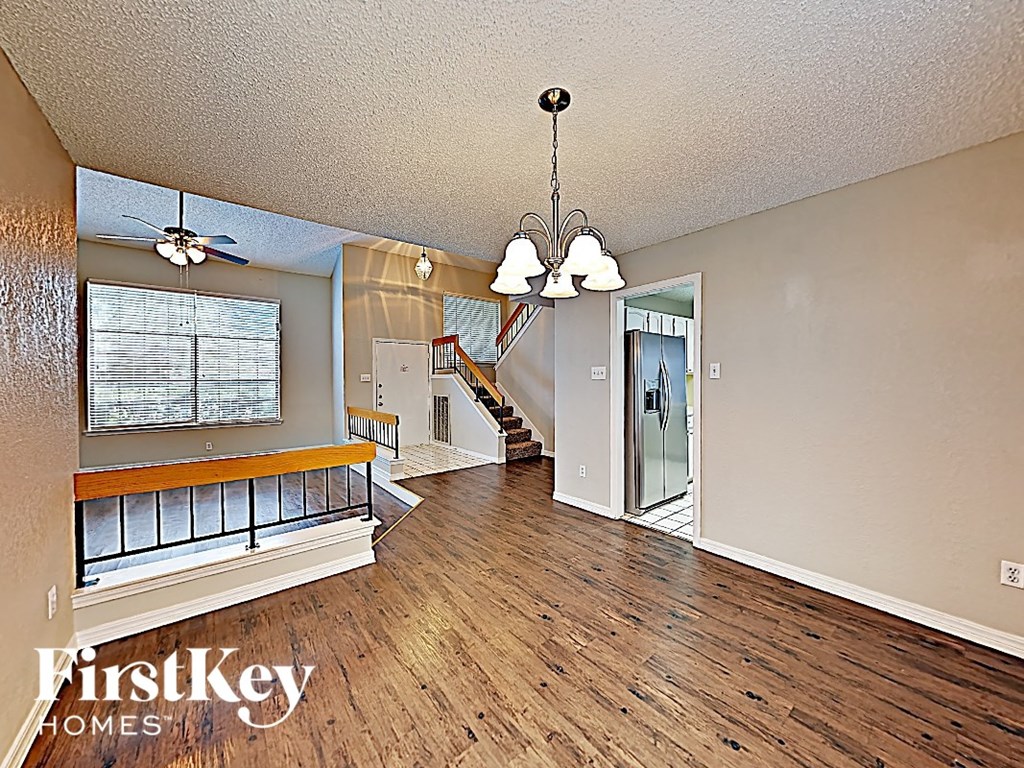 A spacious living room with wood flooring and a staircase in the background.