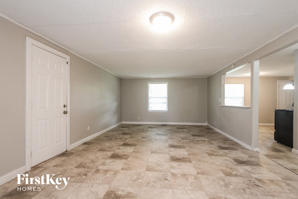 A spacious empty room with a tiled floor and a door on the left.