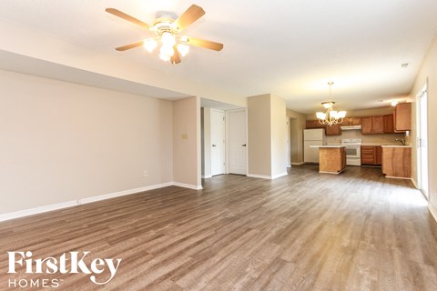 an empty living room with a ceiling fan and a kitchen