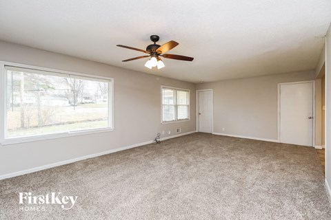 A spacious room with a ceiling fan and two windows.