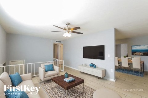 A living room with a white couch, a coffee table, and a flat screen TV mounted on the wall.