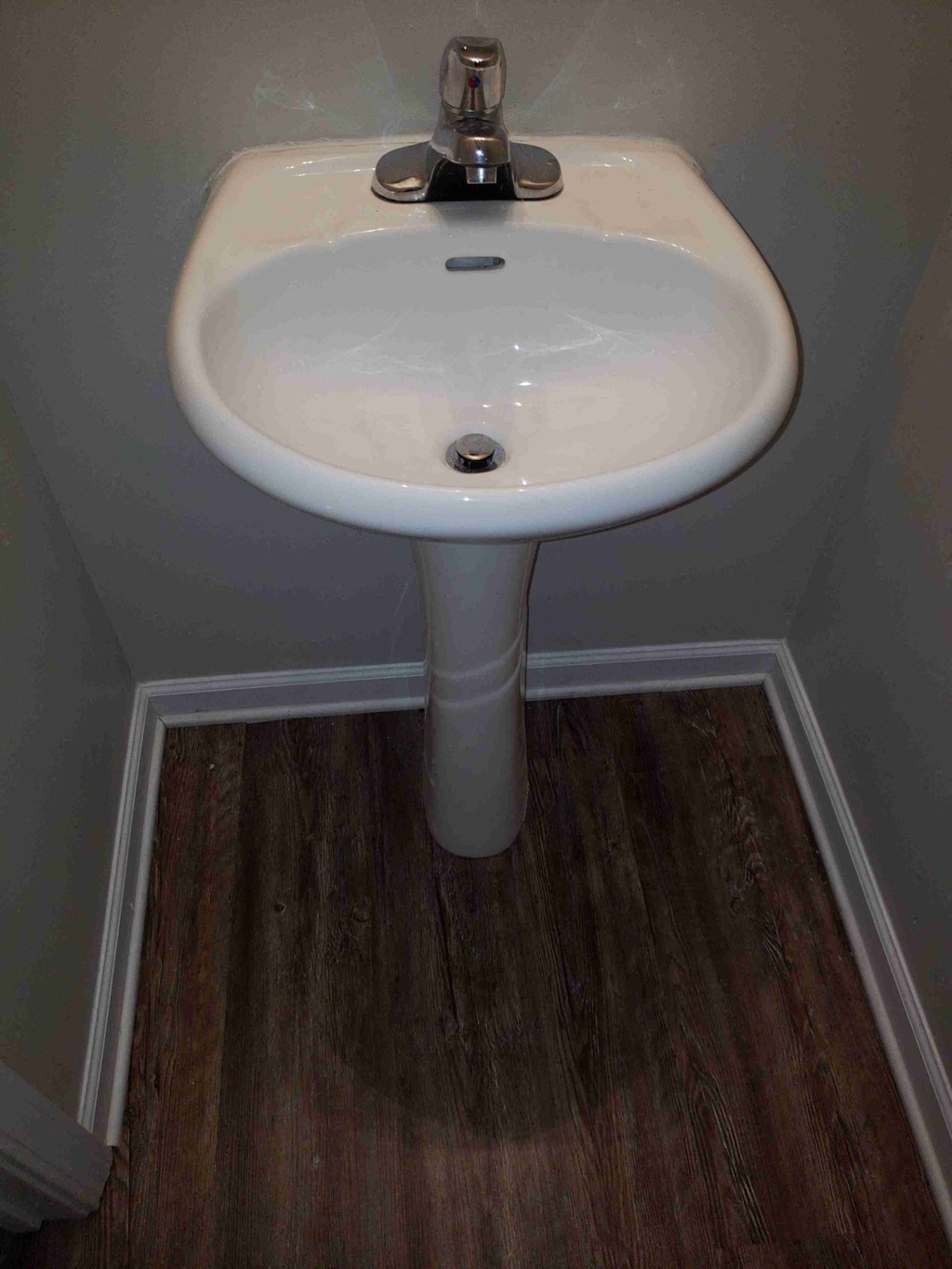 a white pedestal sink in a bathroom with wooden floors
