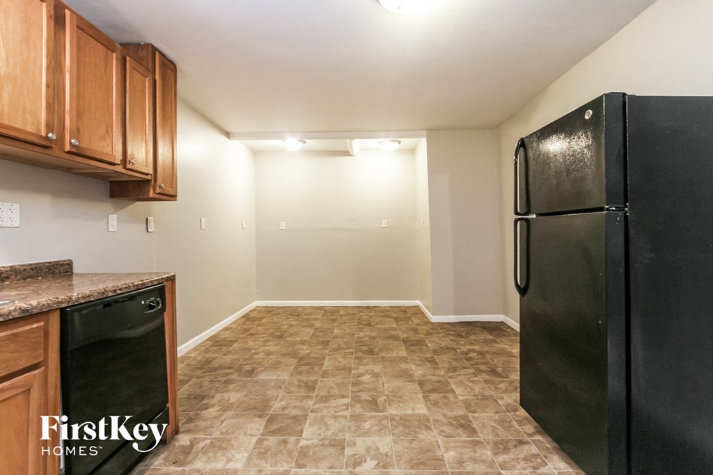 A kitchen with a black fridge, brown cabinets and a brown tiled floor.