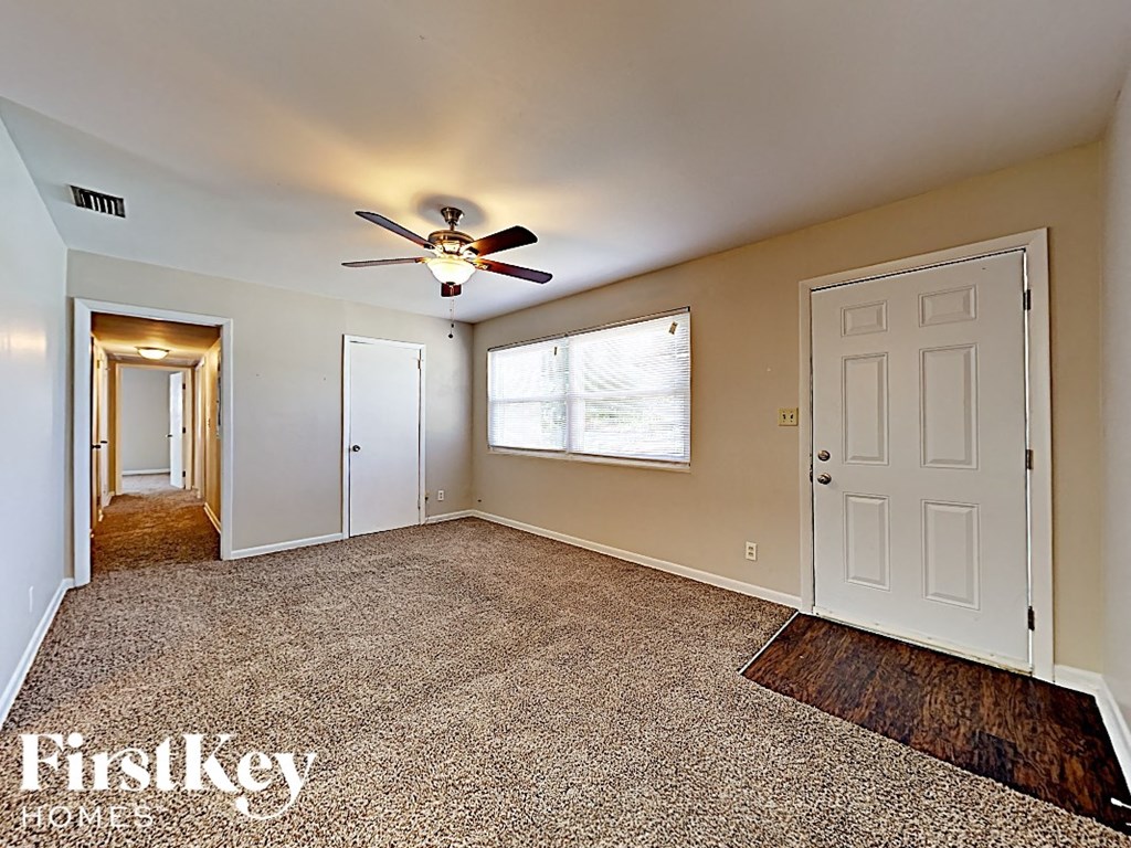 an empty living room with a ceiling fan and a door to a hallway