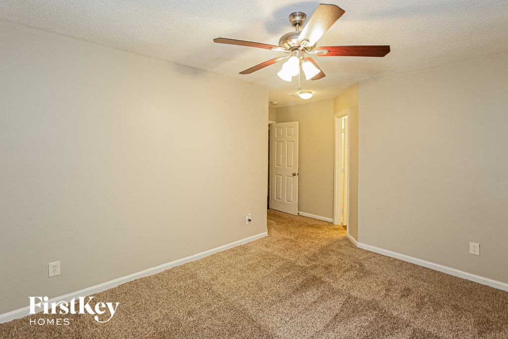 A carpeted room with a ceiling fan and a door.