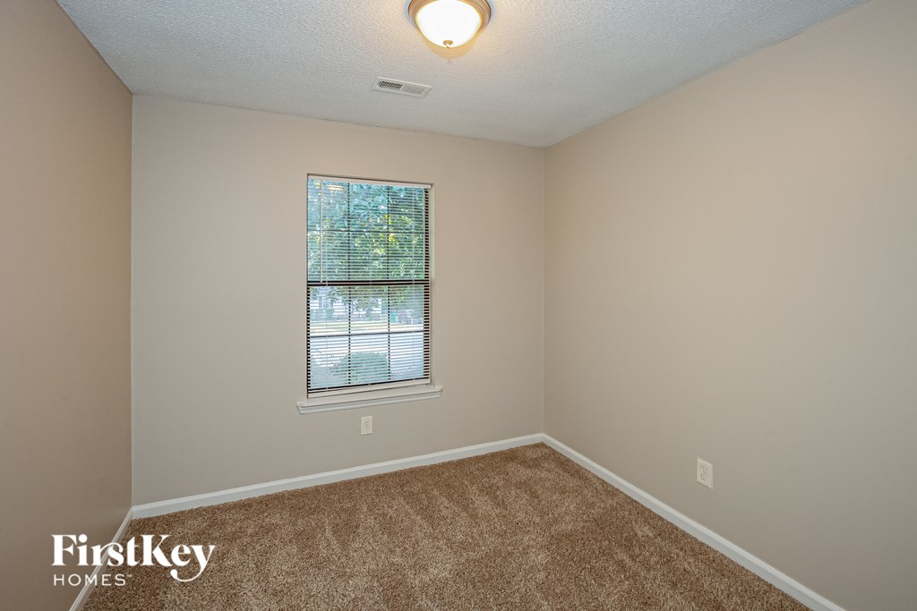 A room with a carpeted floor and a window with blinds.