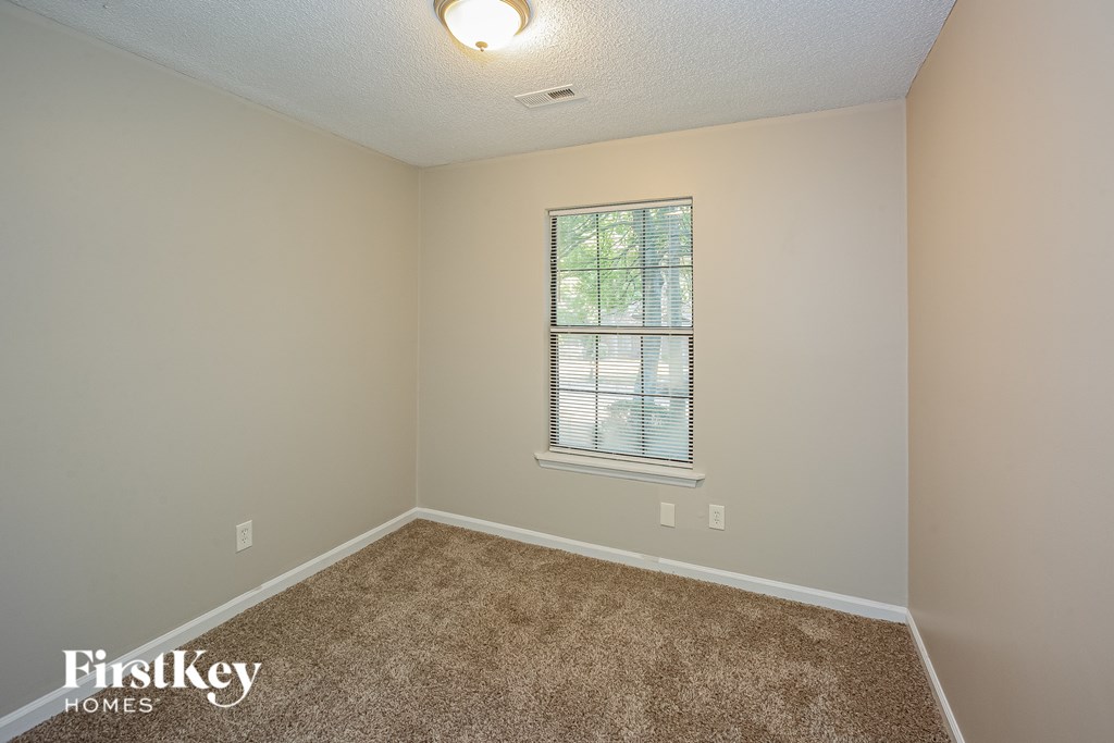 A room with a carpeted floor and a window with blinds.