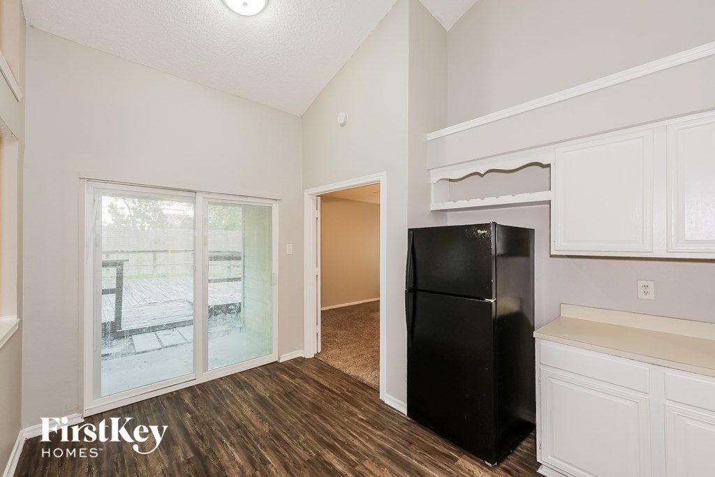A black fridge in a kitchen with white cabinets and a wooden floor.