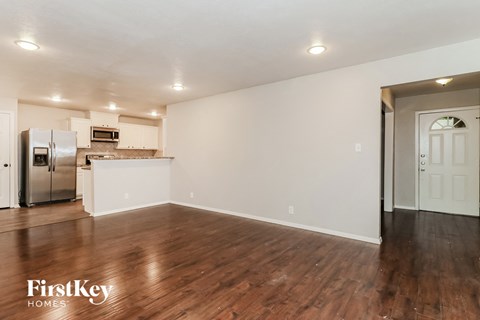 an empty living room and kitchen with wood flooring and white walls