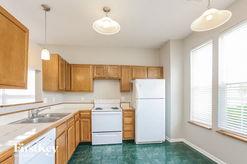 a kitchen with white appliances and wood cabinets and green flooring