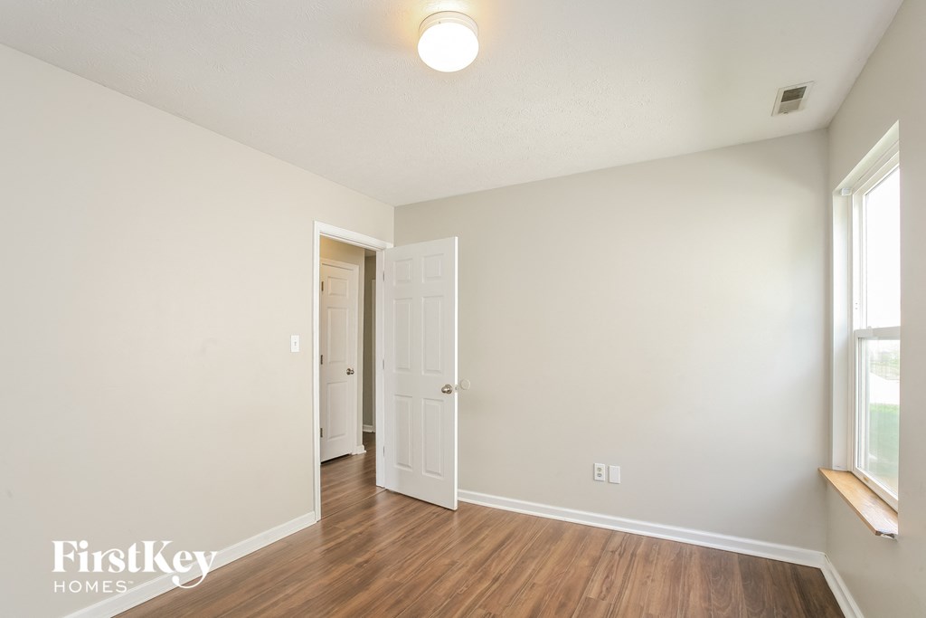 a living room with white walls and wood flooring and a door to a hallway