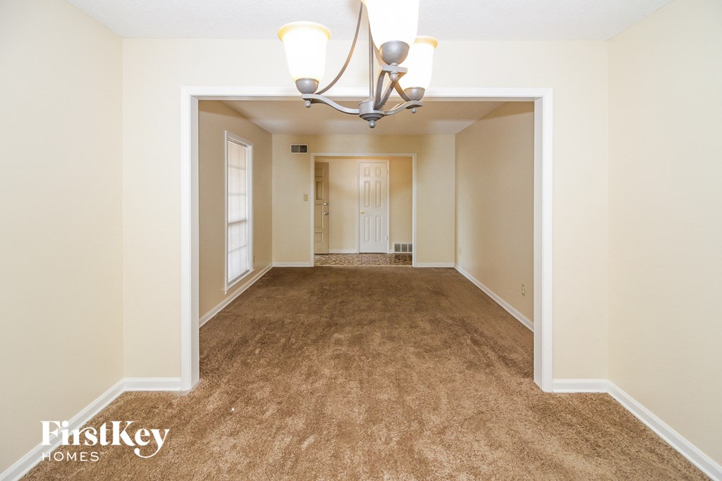 A spacious room with a carpeted floor and a chandelier hanging from the ceiling.