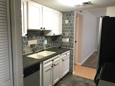 A kitchen with white cabinets and a black counter top.