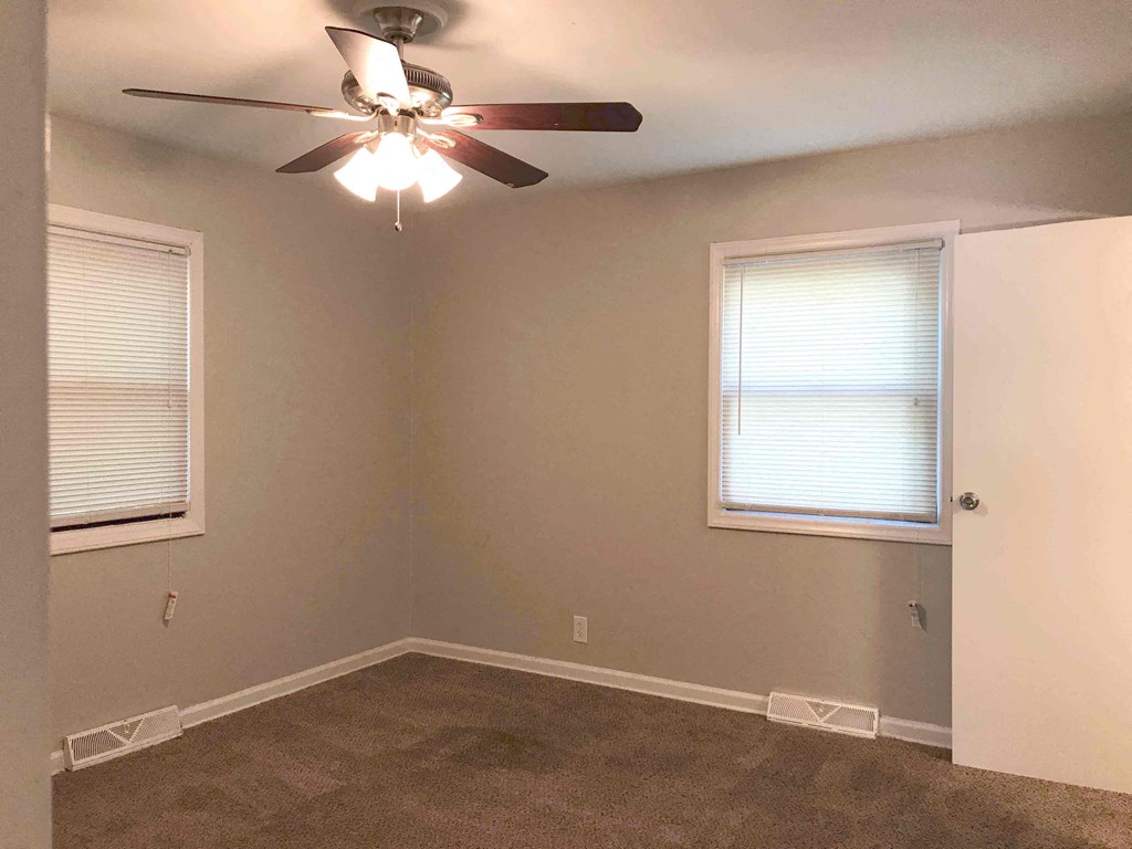 an empty room with a ceiling fan and two windows