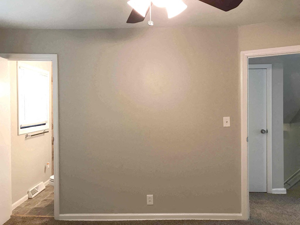 a room with a white wall and a door and a ceiling fan