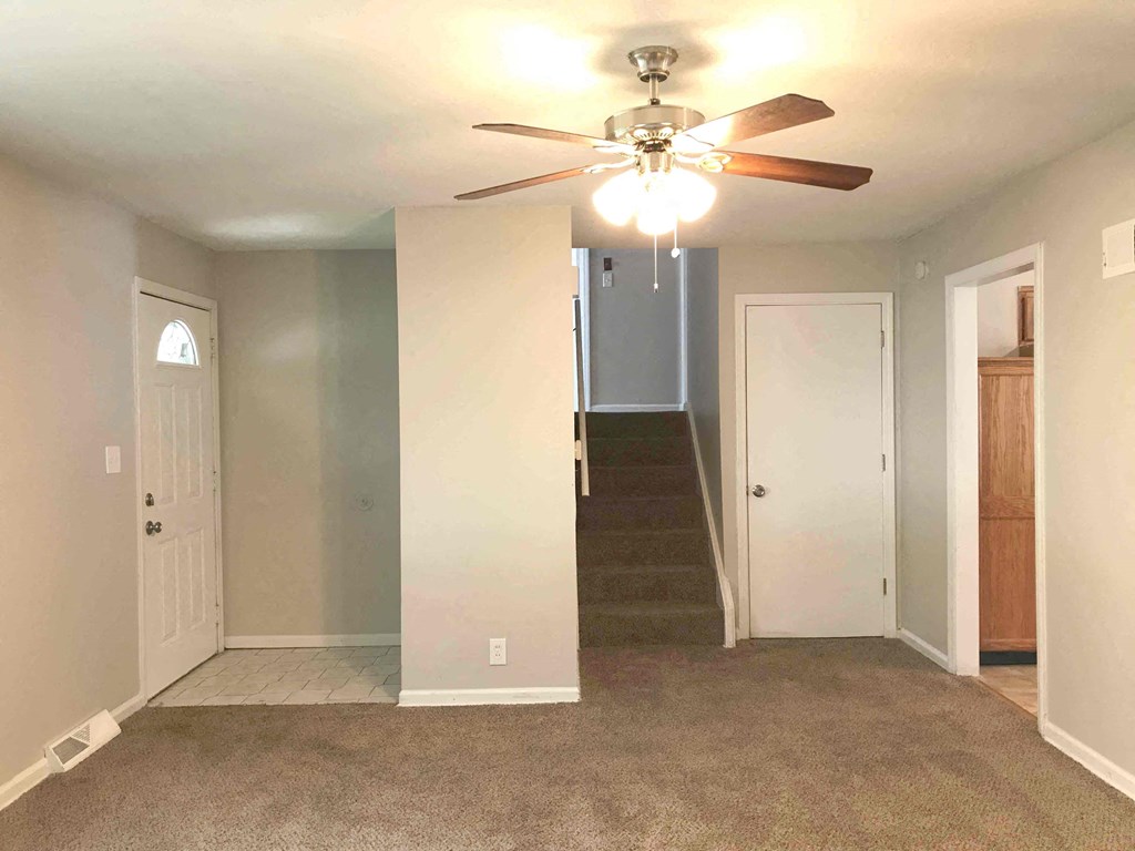 an empty living room with a ceiling fan and a staircase