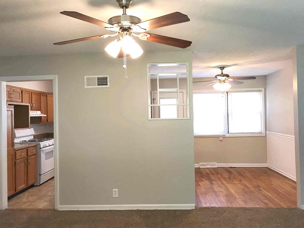 an empty living room with a ceiling fan and a kitchen