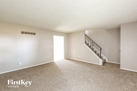 A spacious empty room with a staircase leading to the second floor.