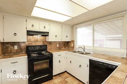 A kitchen with a black stove top oven, white cabinets, and a black dishwasher.