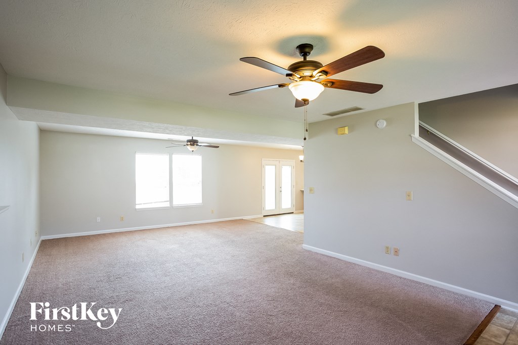 an empty living room with a ceiling fan and white walls