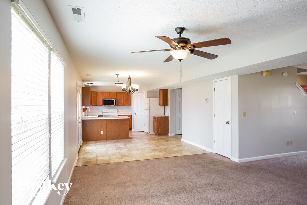an empty living room with a ceiling fan and a kitchen
