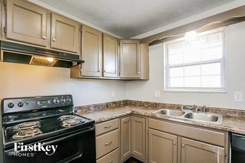 A kitchen with a black stove top oven and beige cabinets.