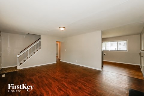 A spacious room with wooden floors and a staircase on the left side.