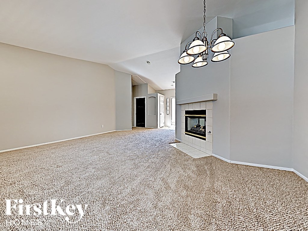 A large, empty room with a fireplace and a carpeted floor.