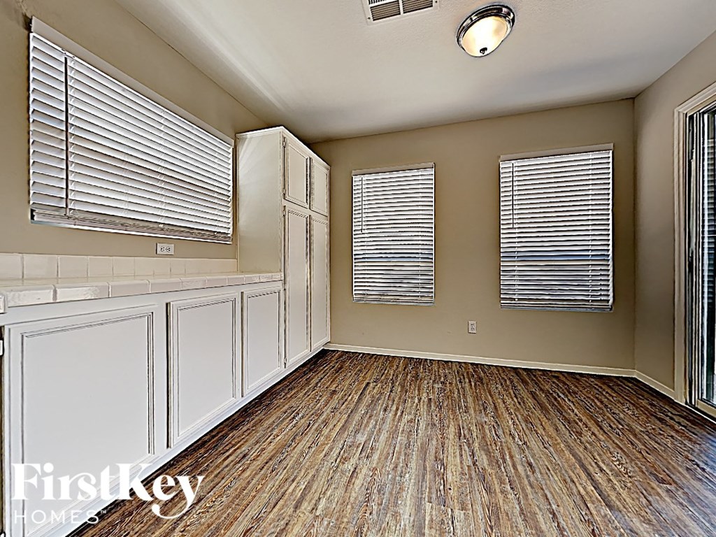 A room with wooden flooring and two windows with blinds.