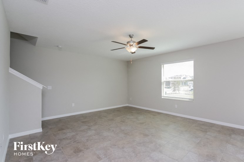 A spacious empty room with a ceiling fan and a window.