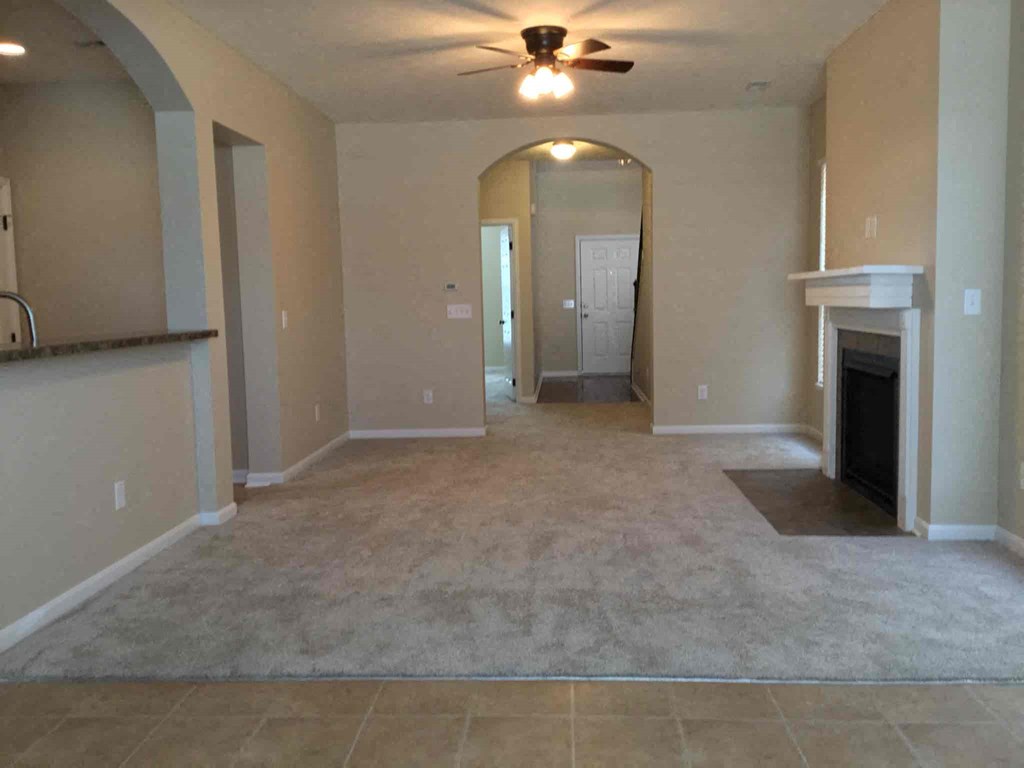 an empty living room with a ceiling fan and a fireplace