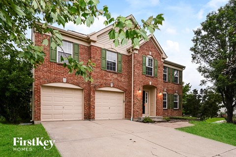 A brick house with a garage and a tree in front.