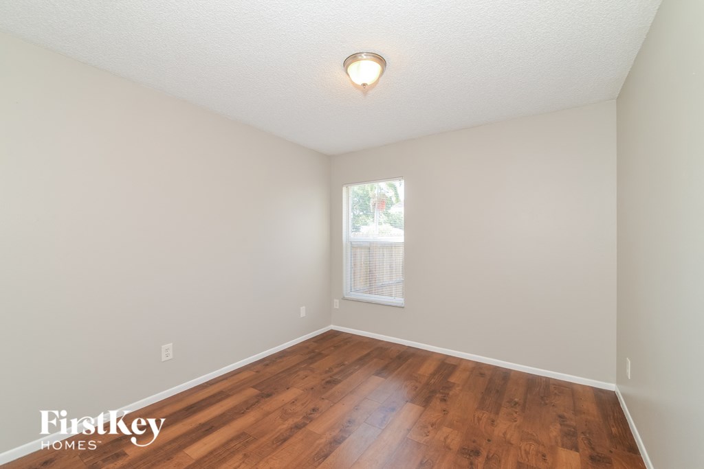 a bedroom with hardwood floors and white walls and a window