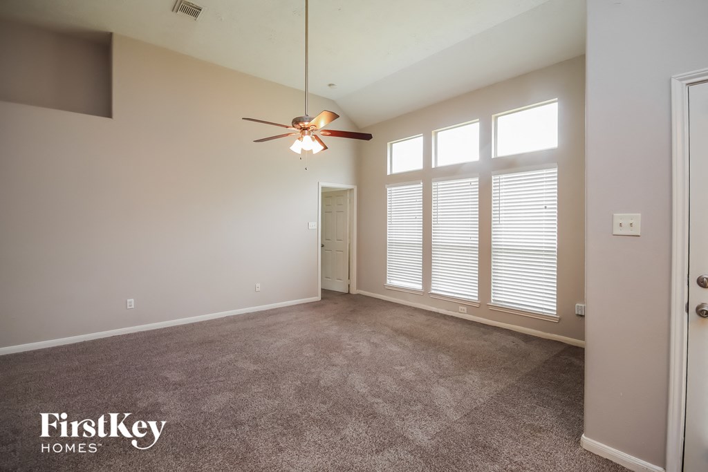 an empty living room with a ceiling fan and large windows