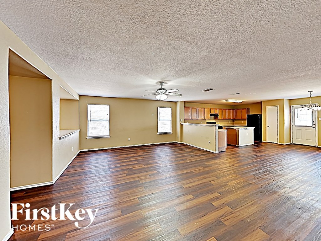 A spacious room with wooden flooring and a kitchen area in the background.