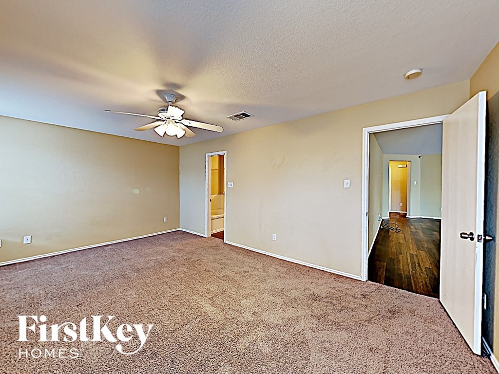 A spacious room with a ceiling fan and a door leading to another room.