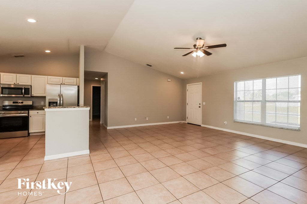 A spacious room with a ceiling fan and a kitchen area in the background.