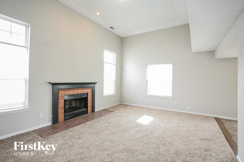 A spacious living room with a fireplace and two windows.