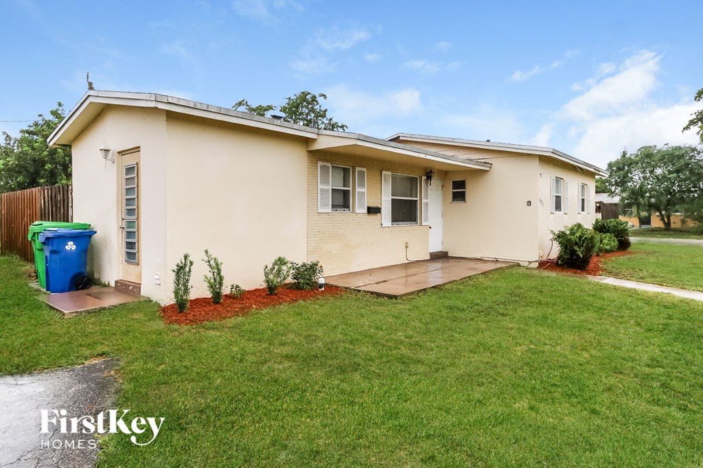 a small white house with a lawn and a blue trash can