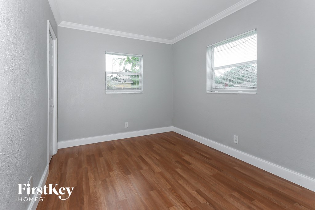 a bedroom with wood floors and grey walls and two windows
