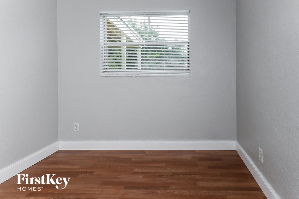 the bedroom of a small rental house with wood floors and a window