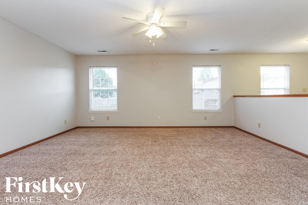 A spacious room with a carpeted floor and a ceiling fan.