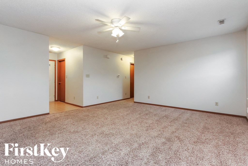 A carpeted room with a ceiling fan and two doors.