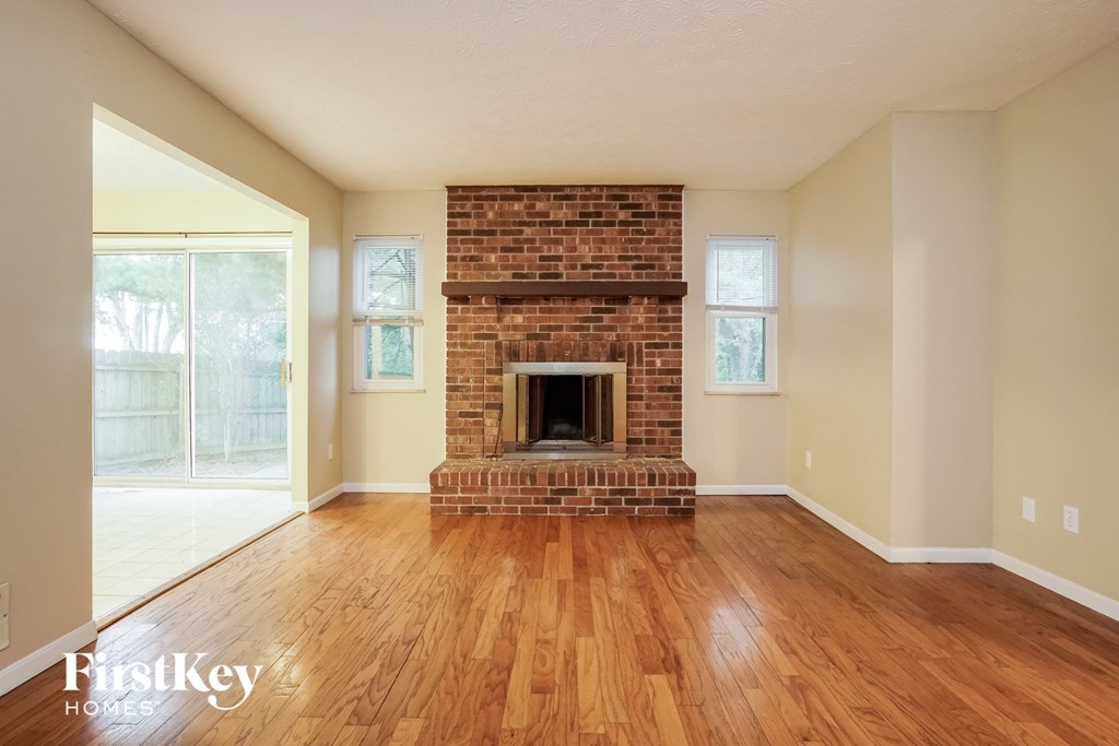 an empty living room with a brick fireplace and wooden floors